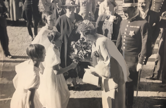 Nuori tyttö ojentaa kukkia Norjan kruununprinsessalle mustavalkoisessa valokuvassa.