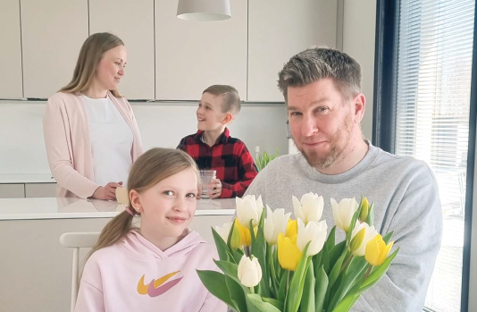 Nelihenkinen perhe hymyilee vaaleassa keittiössä.